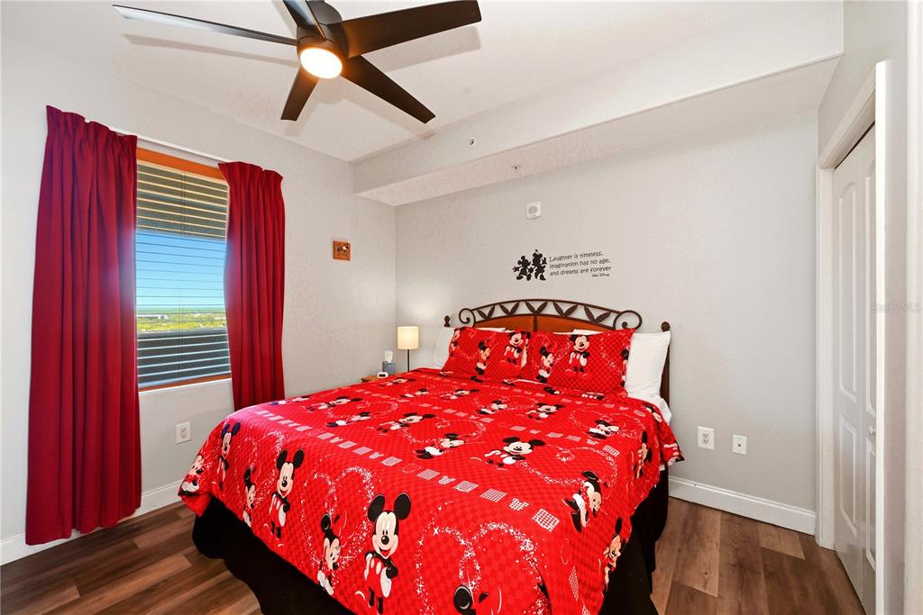 A bedroom features a Mickey Mouse-themed bedspread, red curtains, and a ceiling fan — 13415 BLUE HERON BEACH DRIVE UNIT 1408, ORLANDO, FL