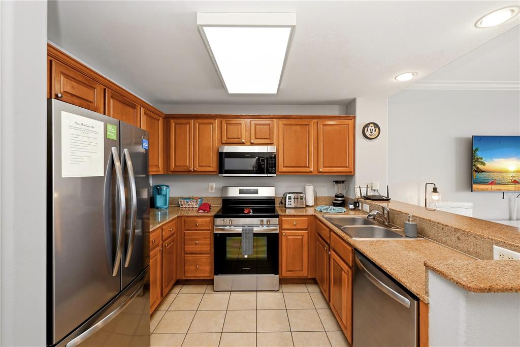 A kitchen features wood cabinets, stainless steel appliances, granite countertops, and tile flooring — 13415 BLUE HERON BEACH DRIVE UNIT 1408, ORLANDO, FL