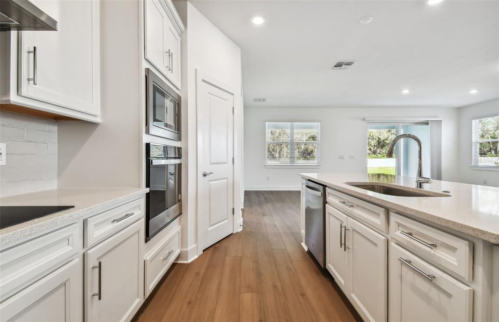 A modern kitchen features white cabinets, stainless steel appliances, and wood-look flooring — 9944 JOHNSON OAKS GLEN, PARRISH, FL
