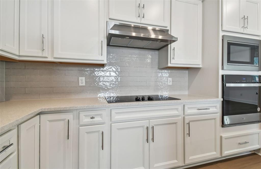 A kitchen features white cabinets, stainless steel appliances, a glass cooktop, and a tiled backsplash — 9944 JOHNSON OAKS GLEN, PARRISH, FL