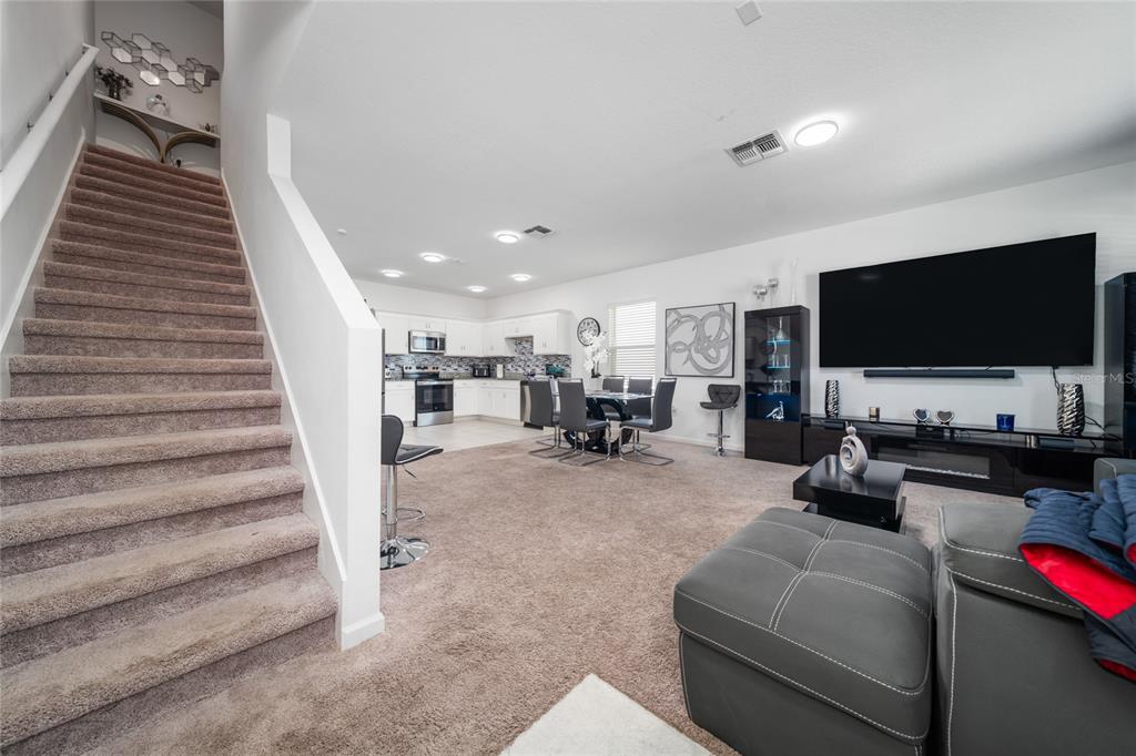 An open-concept living room and kitchen area features carpeted stairs, a large television, and dining furniture — 386 CADBERRY PLACE, ST CLOUD, FL