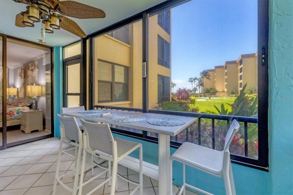 A screened-in balcony with a high-top table, four chairs, and a view of apartment buildings — 8776 MIDNIGHT PASS ROAD UNIT C107, SARASOTA, FL
