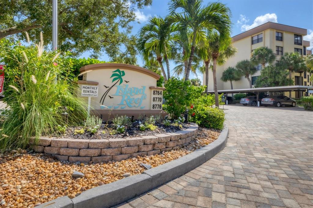 A stone sign for Island Reef stands in front of a multi-story apartment building — 8776 MIDNIGHT PASS ROAD UNIT C107, SARASOTA, FL