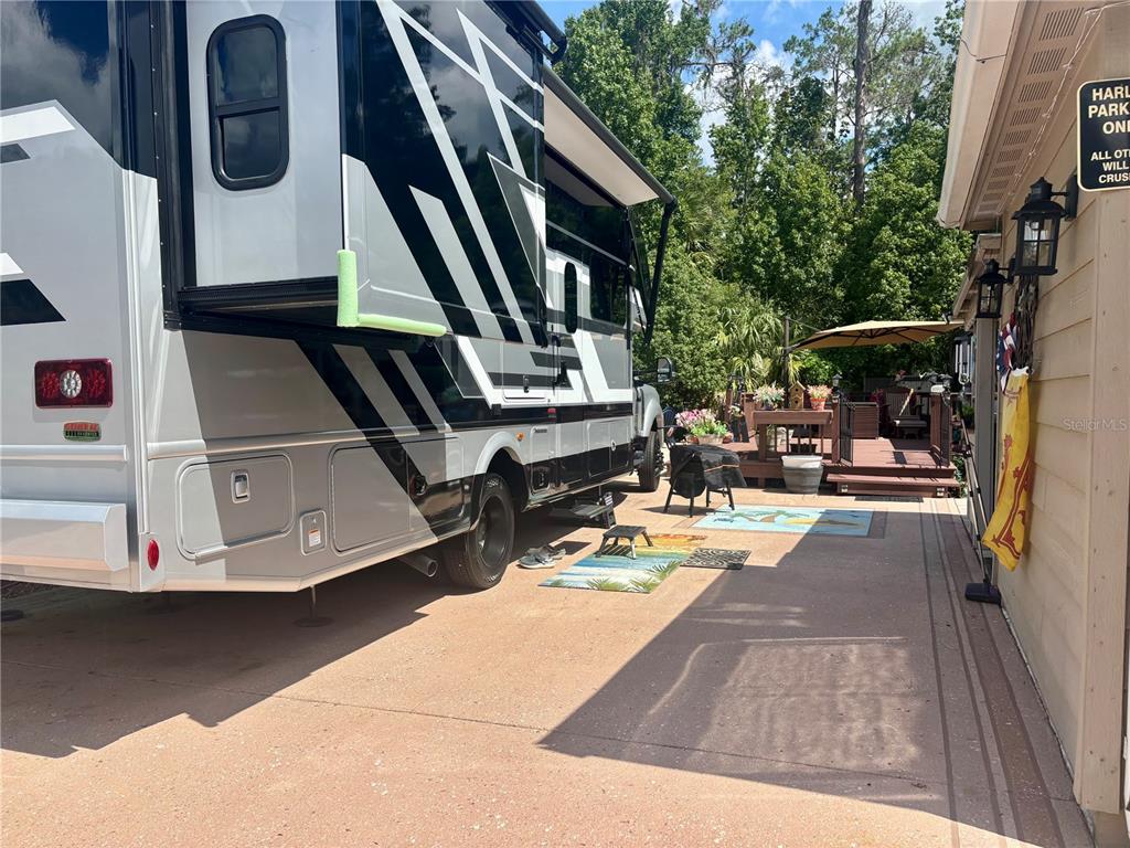 A large recreational vehicle is parked on a concrete driveway next to a wooden deck — 10371 NE 28TH LOOP, SILVER SPRINGS, FL