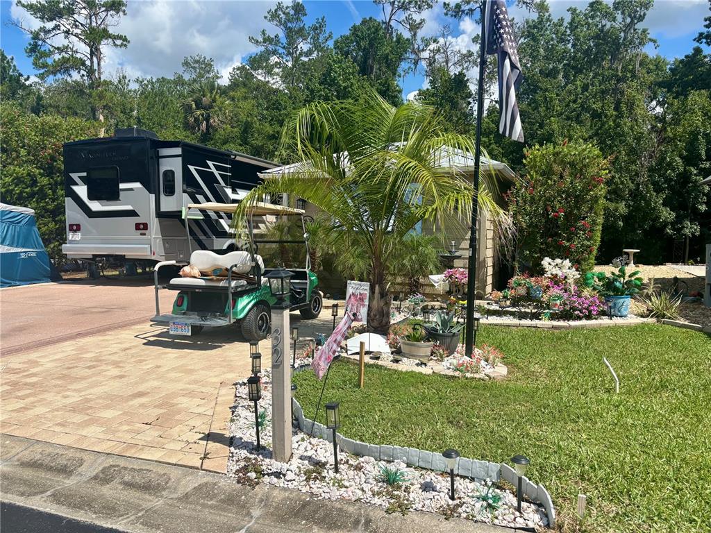 A house exterior features a paved driveway with a parked RV, golf cart, and landscaping — 10371 NE 28TH LOOP, SILVER SPRINGS, FL