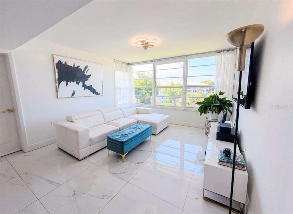 A bright living room features a white sectional sofa, blue ottoman, and polished tile floors — 3635 WHITEHALL DRIVE UNIT 401, WEST PALM BEACH, FL