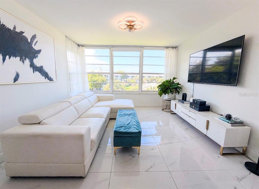 A bright living room features a white sectional sofa, blue ottoman, and large wall-mounted television — 3635 WHITEHALL DRIVE UNIT 401, WEST PALM BEACH, FL
