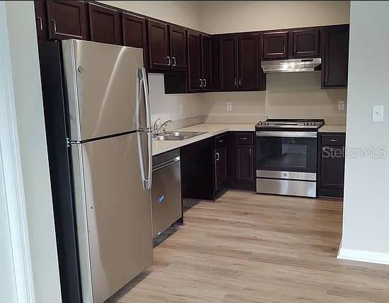 A kitchen features dark wood cabinets, stainless steel appliances, and light-colored wood-look flooring — 2609 LANDOVER BOULEVARD UNIT 2617, SPRING HILL, FL