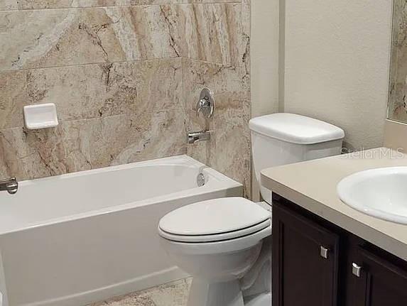 A bathroom features a white bathtub with tan marble-look tile walls, a toilet, and a vanity — 2609 LANDOVER BOULEVARD UNIT 2617, SPRING HILL, FL