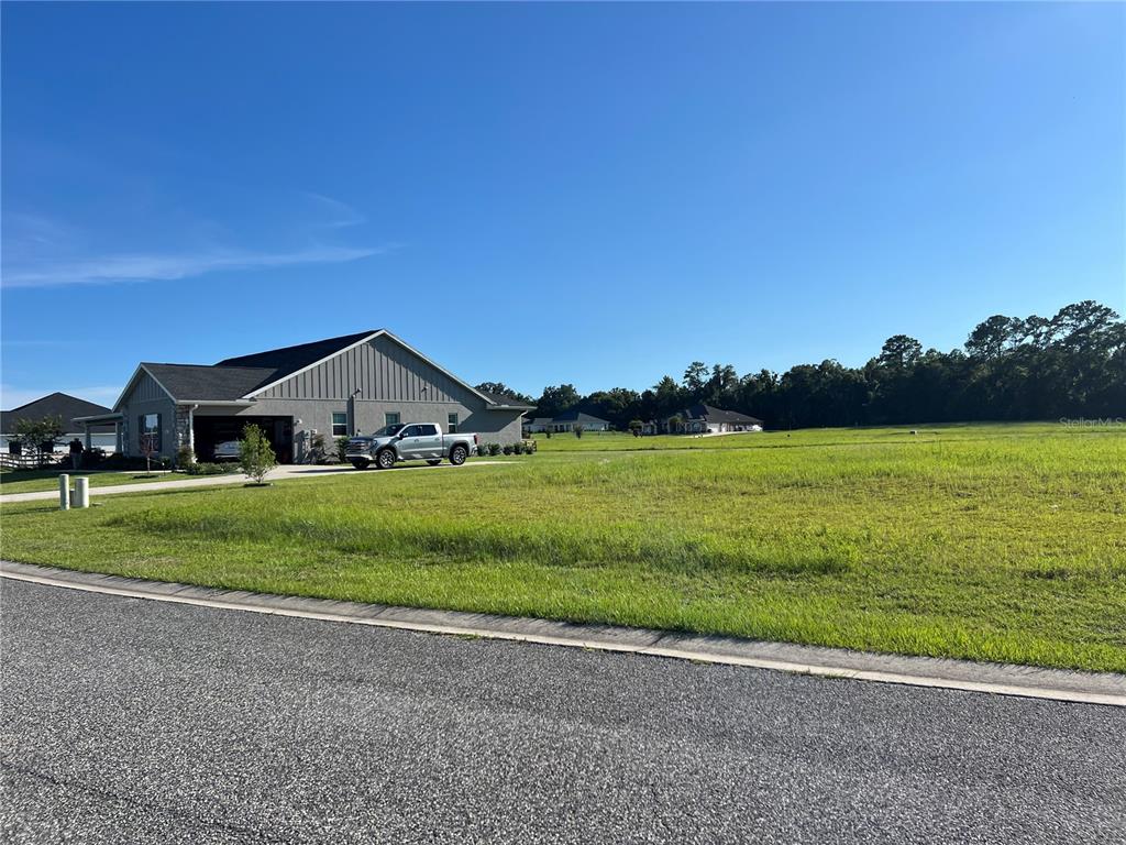 A large, grassy vacant lot sits next to a modern single-story house with a driveway — 000 NW 79TH LOOP, OCALA, FL