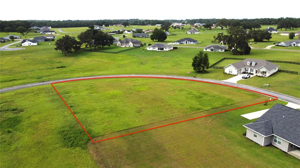 An aerial view shows a vacant, trapezoidal residential lot outlined in red along a paved road — 000 NW 79TH LOOP, OCALA, FL