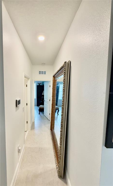 A hallway with light tile flooring, white walls, and a large ornate floor mirror — 2098 GOLD DUST DRIVE, MINNEOLA, FL