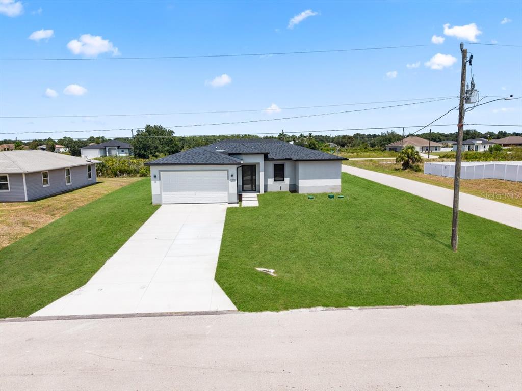 A single-story house with a white garage and dark roof sits on a grassy lot — 2700 69TH ST W, LEHIGH ACRES, FL
