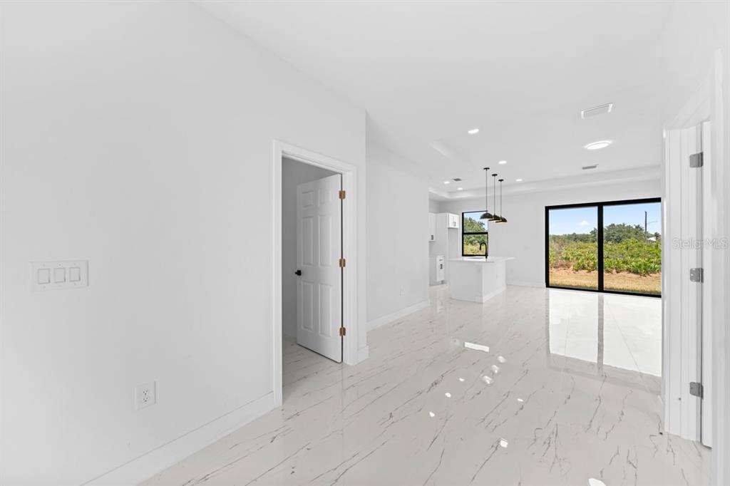 A bright, white-tiled room leads to an open kitchen with pendant lighting and sliding doors — 2700 69TH ST W, LEHIGH ACRES, FL