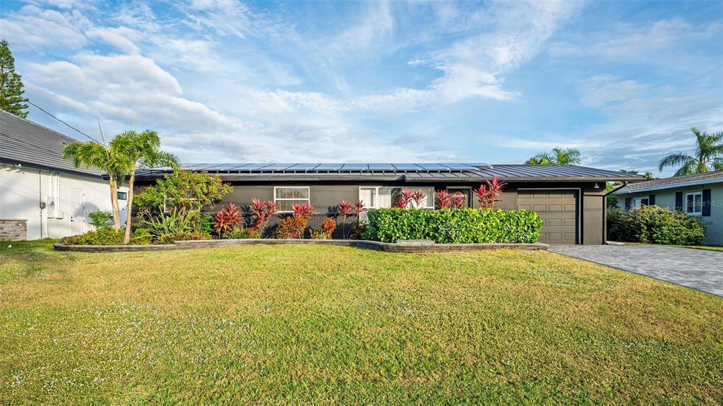 A single-story house with a dark exterior, solar panels on the roof, and landscaped front yard — 113 DELEON ROAD, COCOA BEACH, FL