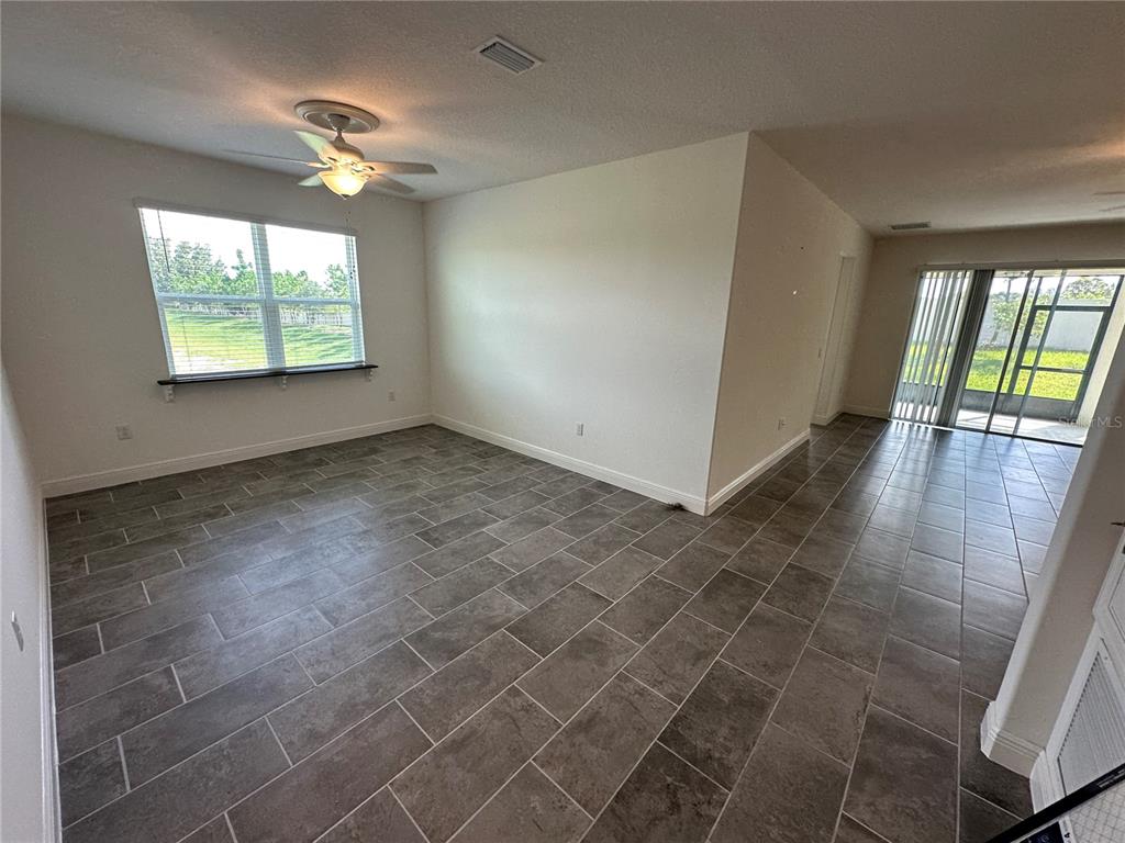 An open-concept room features gray tile flooring, a ceiling fan, and sliding glass patio doors — 484 SHADOW GORGE WAY, EUSTIS, FL