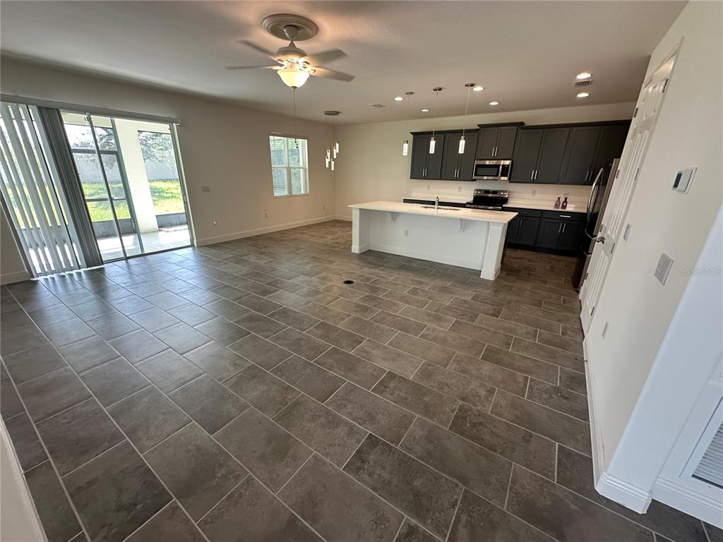 An open-concept kitchen and living area features dark cabinets, a white island, and tiled floors — 484 SHADOW GORGE WAY, EUSTIS, FL