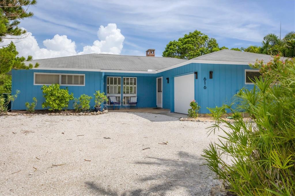 A blue, single-story house with a gravel driveway and a white garage door — 616 LYONS LANE, LONGBOAT KEY, FL