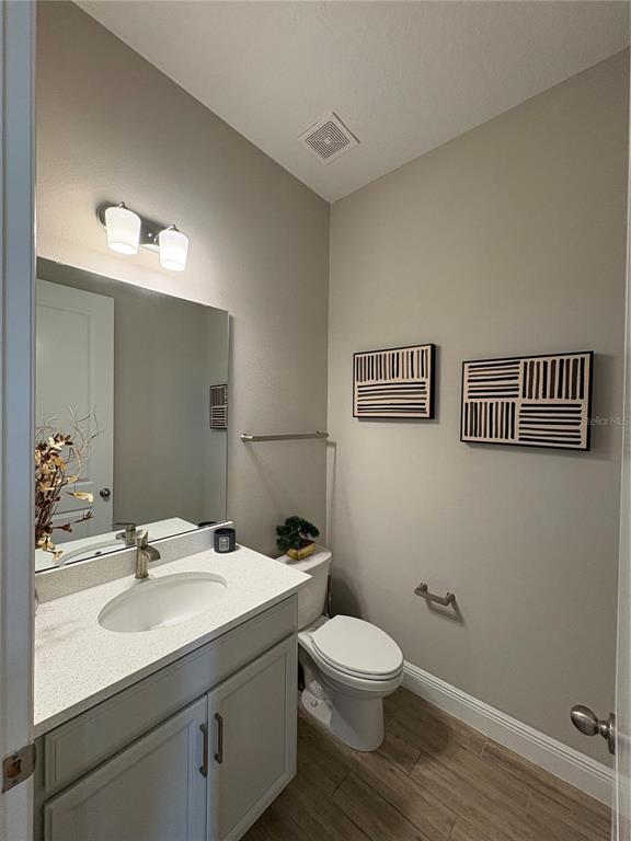 A small bathroom features a vanity with a white countertop, toilet, and two wall artworks — 6553 CYRILS DRIVE, ST CLOUD, FL