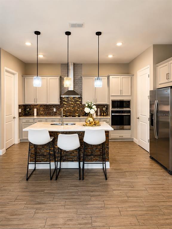 A kitchen features a central island with three stools, light cabinetry, and a stone backsplash — 6553 CYRILS DRIVE, ST CLOUD, FL