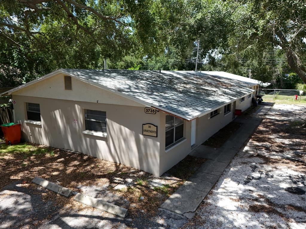 An exterior view of a single-story apartment building with a light-colored facade and shingled roof — 3735 141ST PLACE, LARGO, FL