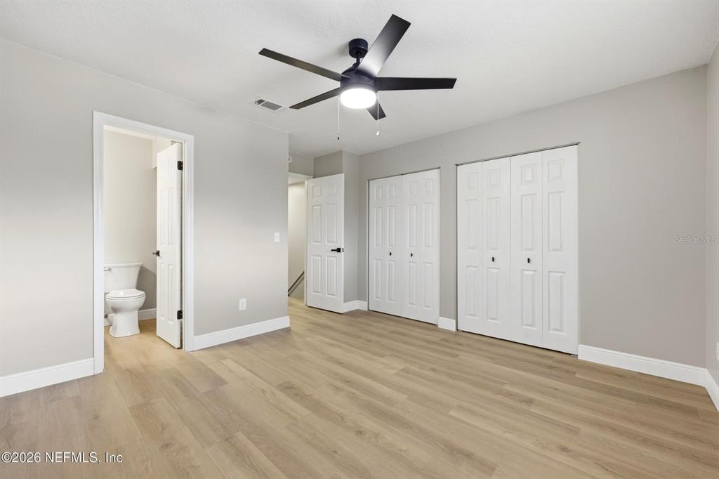 A bedroom features light wood-look flooring, gray walls, a ceiling fan, and two closet doors — 3801 CROWN POINT ROAD UNIT 2093, JACKSONVILLE, FL