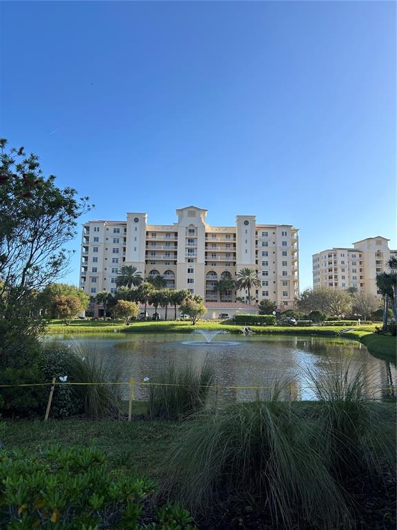 A multi-story residential building stands behind a pond with a fountain and landscaped grounds — 261 MINORCA BEACH WAY UNIT 203, NEW SMYRNA BEACH, FL