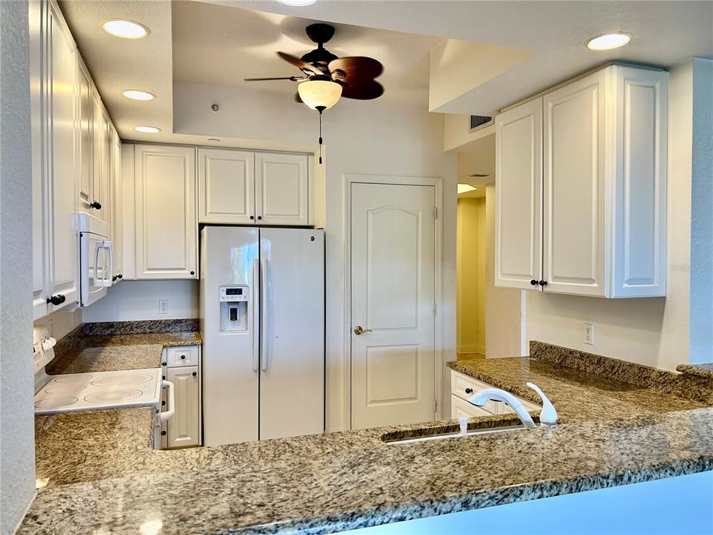 A kitchen features white cabinets, granite countertops, a white refrigerator, and a ceiling fan — 261 MINORCA BEACH WAY UNIT 203, NEW SMYRNA BEACH, FL