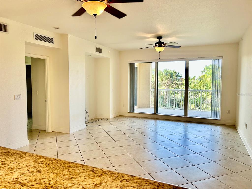 An open living area features tile flooring, two ceiling fans, and a sliding glass door — 261 MINORCA BEACH WAY UNIT 203, NEW SMYRNA BEACH, FL