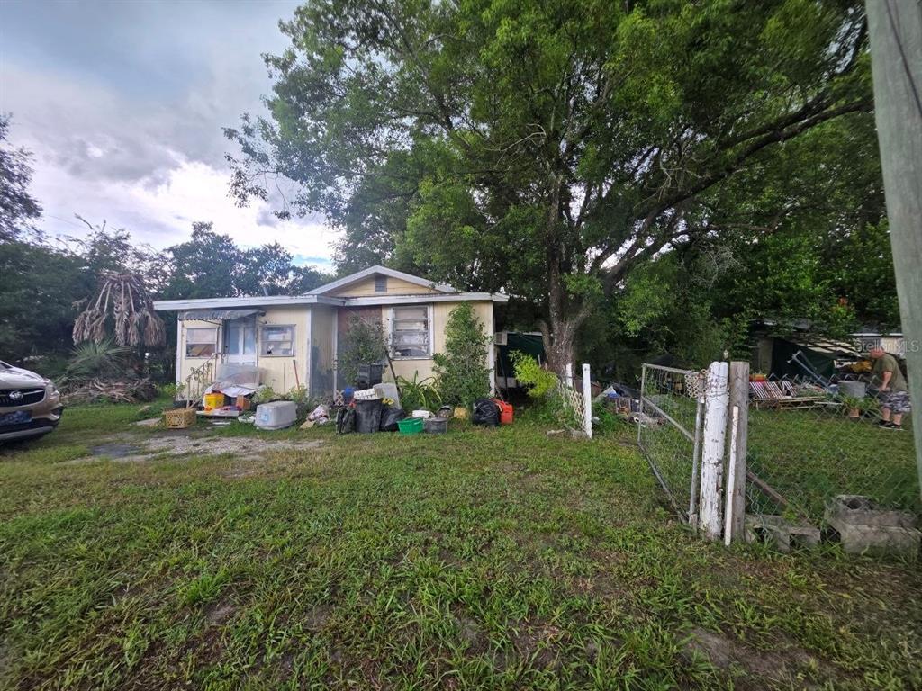 A small, weathered yellow house with a cluttered yard and a chain-link fence — 39521 COIT ROAD, DADE CITY, FL