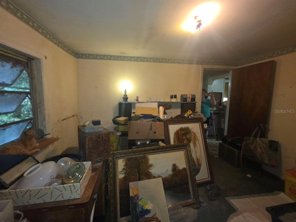 A cluttered room with beige walls, a window, and several framed paintings leaning against furniture — 39521 COIT ROAD, DADE CITY, FL