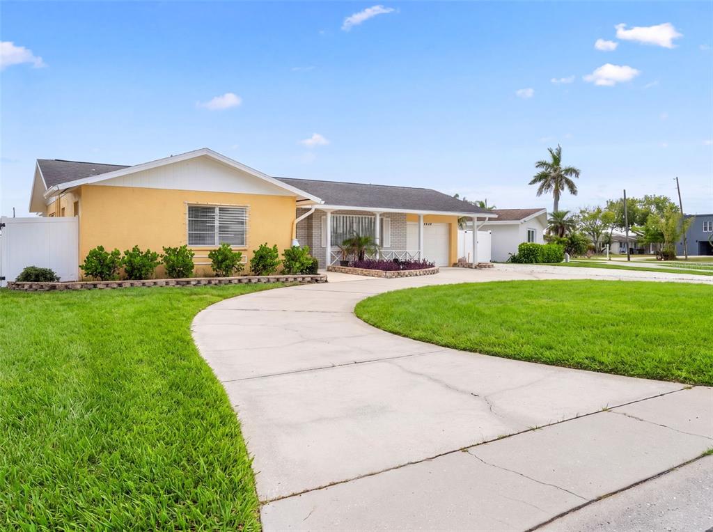 A yellow single-story house features a curved concrete driveway and a white privacy fence — 4608 ARLINGTON ROAD, PALMETTO, FL