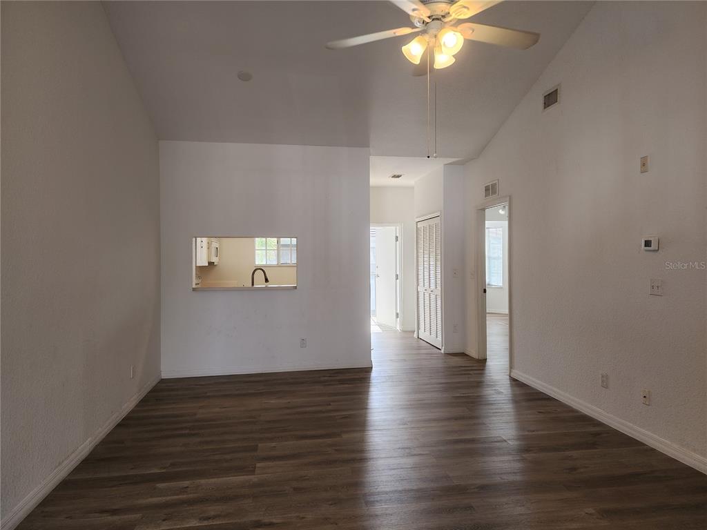 An empty living room features wood-look flooring, a ceiling fan, and a kitchen pass-through window — 8416 BERNWOOD COVE LOOP UNIT 1612, FORT MYERS, FL