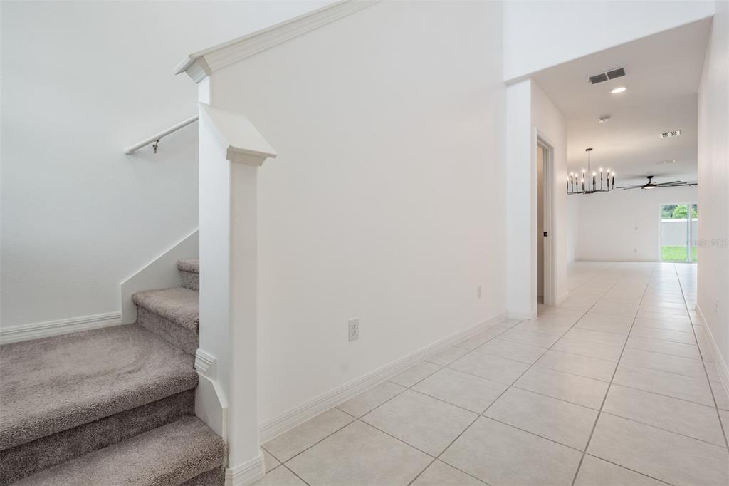 A tiled entryway leads to a carpeted staircase and a bright, open-concept living area — 10112 BRANCHING SHIP TRACE, WESLEY CHAPEL, FL