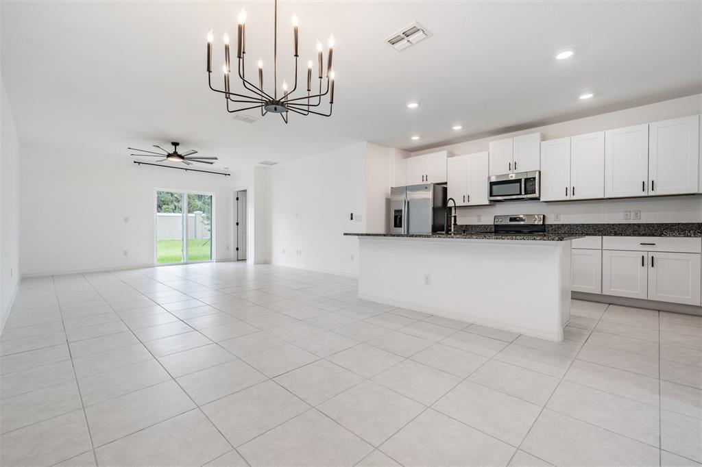 An open-concept kitchen and living area with white cabinets, granite countertops, and tile flooring — 10112 BRANCHING SHIP TRACE, WESLEY CHAPEL, FL