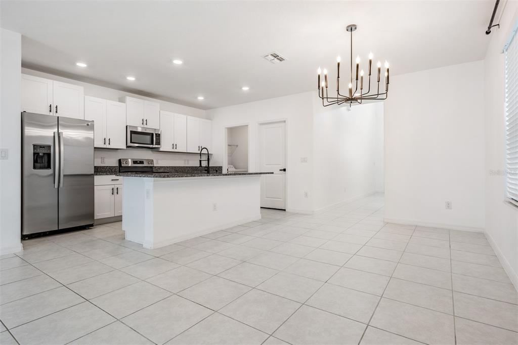 A kitchen with white cabinets, stainless steel appliances, and a granite island overlooks a tiled area — 10112 BRANCHING SHIP TRACE, WESLEY CHAPEL, FL