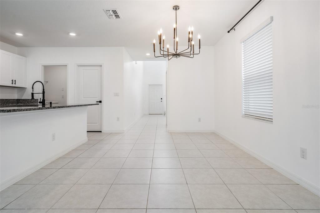 A bright dining area features white walls, tile flooring, and a modern black chandelier — 10112 BRANCHING SHIP TRACE, WESLEY CHAPEL, FL