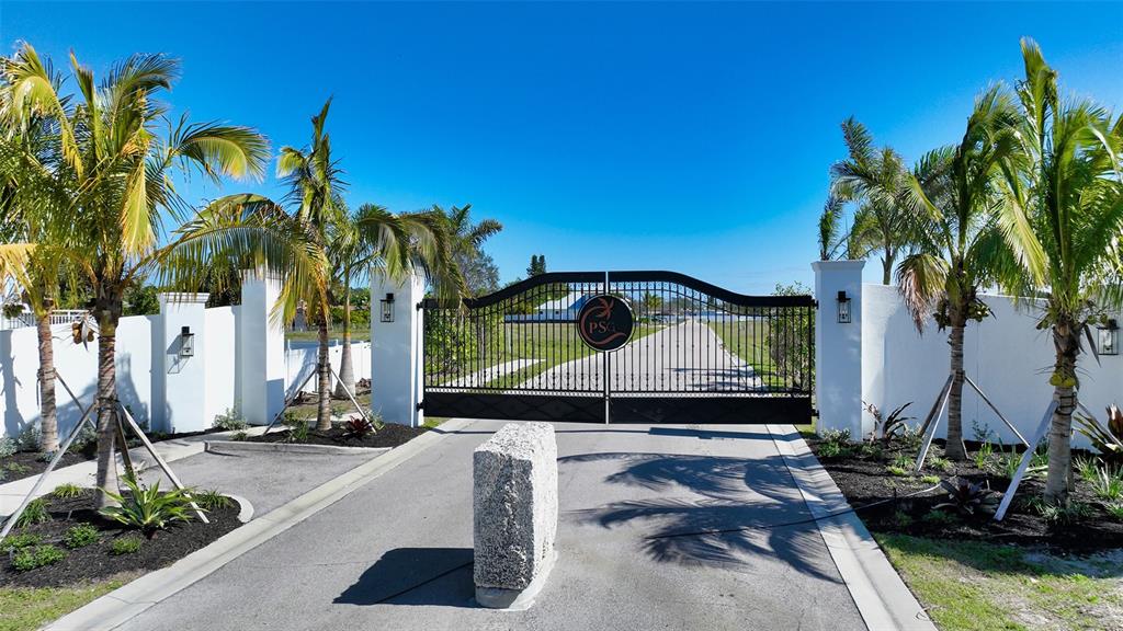 A black metal gate stands between two white pillars surrounded by palm trees — 8001 W 20TH PLACE, BRADENTON, FL