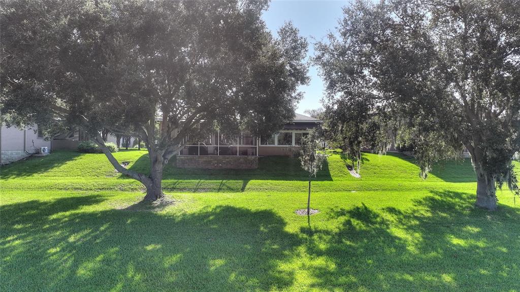A view of a house exterior with a screened-in porch and large trees on a lawn — 492 MEANDERING WAY, POLK CITY, FL