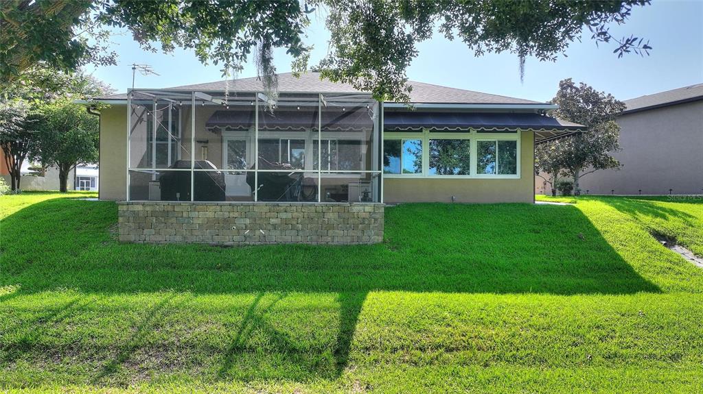 A tan house with a screened-in patio and a stone retaining wall sits on a lawn — 492 MEANDERING WAY, POLK CITY, FL