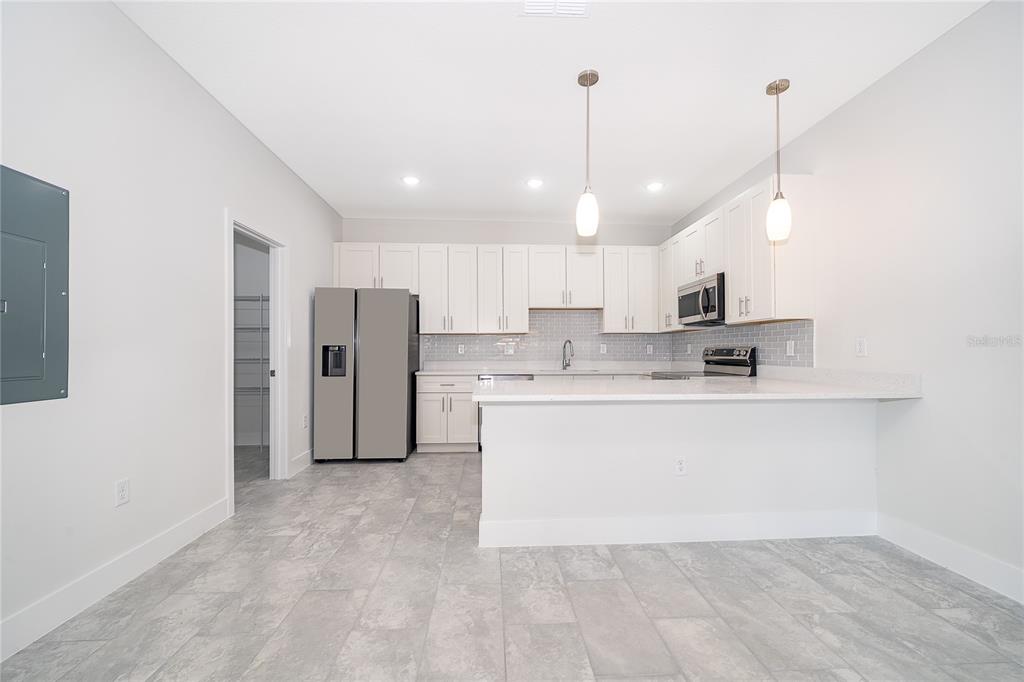 A modern kitchen features white cabinets, stainless steel appliances, a breakfast bar, and tile flooring — 1661 CUMIN DRIVE, KISSIMMEE, FL