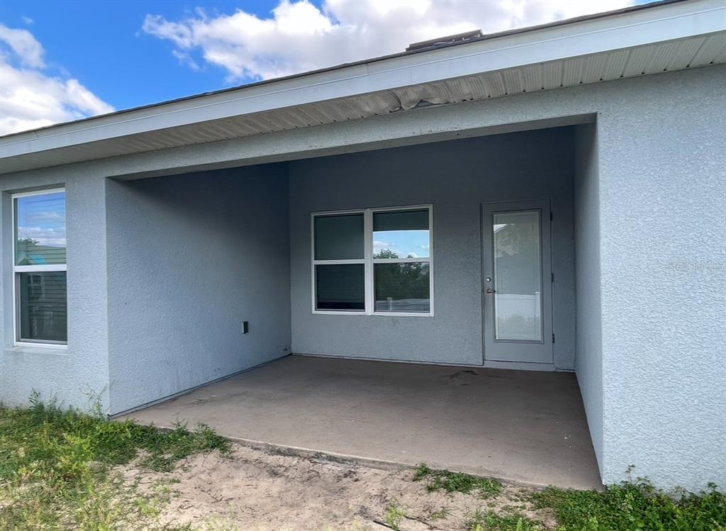 A covered concrete patio features a glass door and a window on a stucco wall — 1295 LEGATTO LOOP, DUNDEE, FL