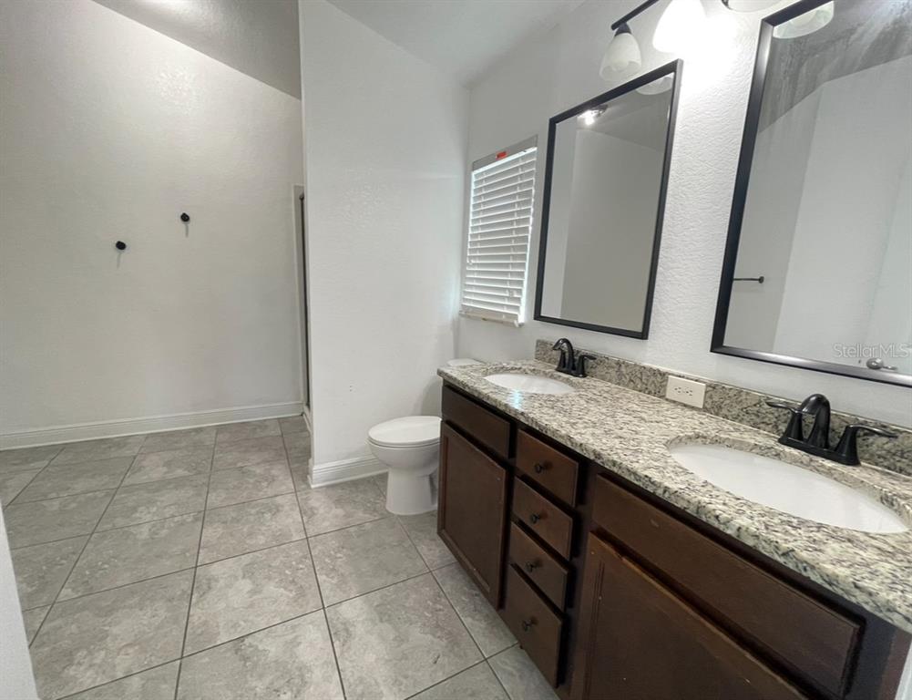 A bathroom features a double vanity with granite countertops, dark wood cabinets, and tiled flooring — 1295 LEGATTO LOOP, DUNDEE, FL