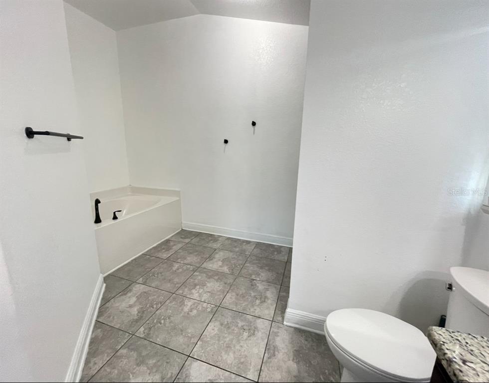 A bathroom features a soaking tub, gray tile flooring, and a toilet — 1295 LEGATTO LOOP, DUNDEE, FL