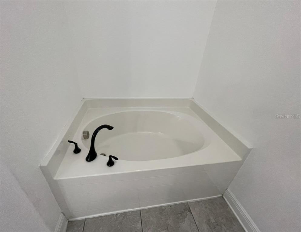 A white built-in soaking tub features black fixtures against plain white walls and tiled flooring — 1295 LEGATTO LOOP, DUNDEE, FL
