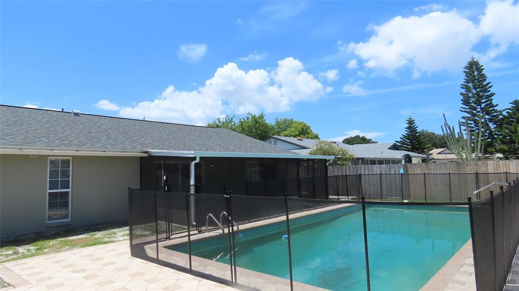 A backyard features a swimming pool with a safety fence and a covered patio area — 2376 MILLWOOD LANE, CLEARWATER, FL
