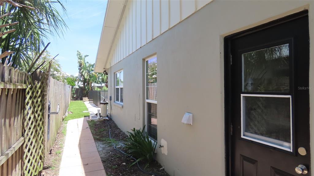 The exterior side of a house features a tan wall, two windows, and a dark door — 2376 MILLWOOD LANE, CLEARWATER, FL
