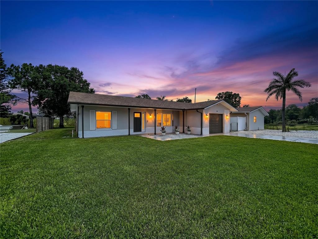 A single-story house with a gray exterior, a dark garage door, and a large lawn — 381 WESTWINDS DRIVE, PALM HARBOR, FL