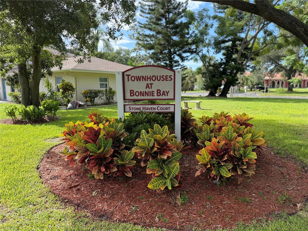 A sign for Townhouses at Bonnie Bay stands in a landscaped garden bed with crotons — 7242 STONE HAVEN COURT N UNIT 7242, PINELLAS PARK, FL
