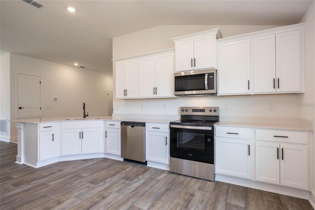 A kitchen features white cabinets, stainless steel appliances, and light countertops over wood-look flooring — 32 RYMSHAW DRIVE, PALM COAST, FL